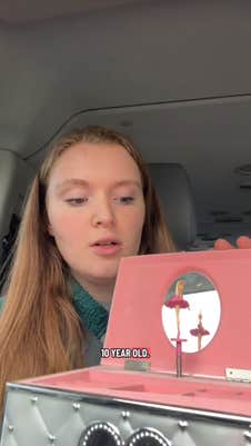 Redheaded woman opening a ballerina music box she bought to show it off. She is staring down into the music box.