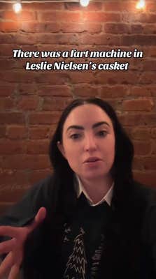 A woman with black hair standing in front of a brick wall, gesturing with her free hand. Text overlay reads, "There was a fart machine in Leslie Nielsen's casket."