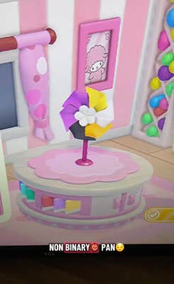 A pinwheel sitting on a platform in a brightly-colored room in the Hello Kitty video game. The pinwheel is in the nonbinary pride flag colors.