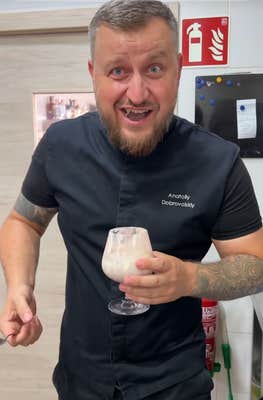 Video of a chef smiling into the camera while holding a cocktail glass full of wine and ice cream.