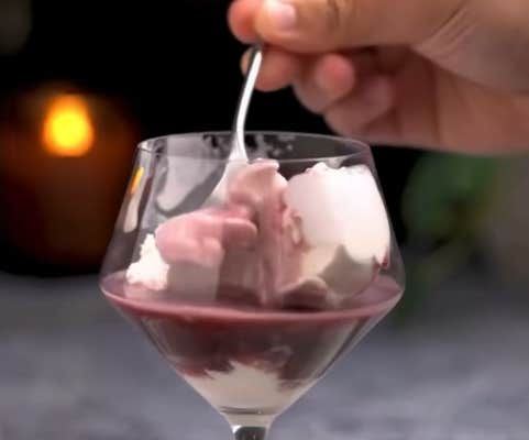 Video showing someone sticking a spoon into a glass of vanilla ice cream and red wine.