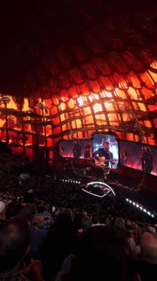 Imagery of a fiery cage crawling with skeletons with Zac Brown dressed with a skeletal crown performing on stage.