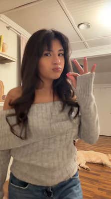 Woman with long hair in an off the shoulder sweater mimicking smoke weed.