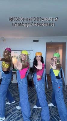 Four women in matching outfits dancing for the camera, the one on the left has a darker skin tone than the other three and blonde hair.